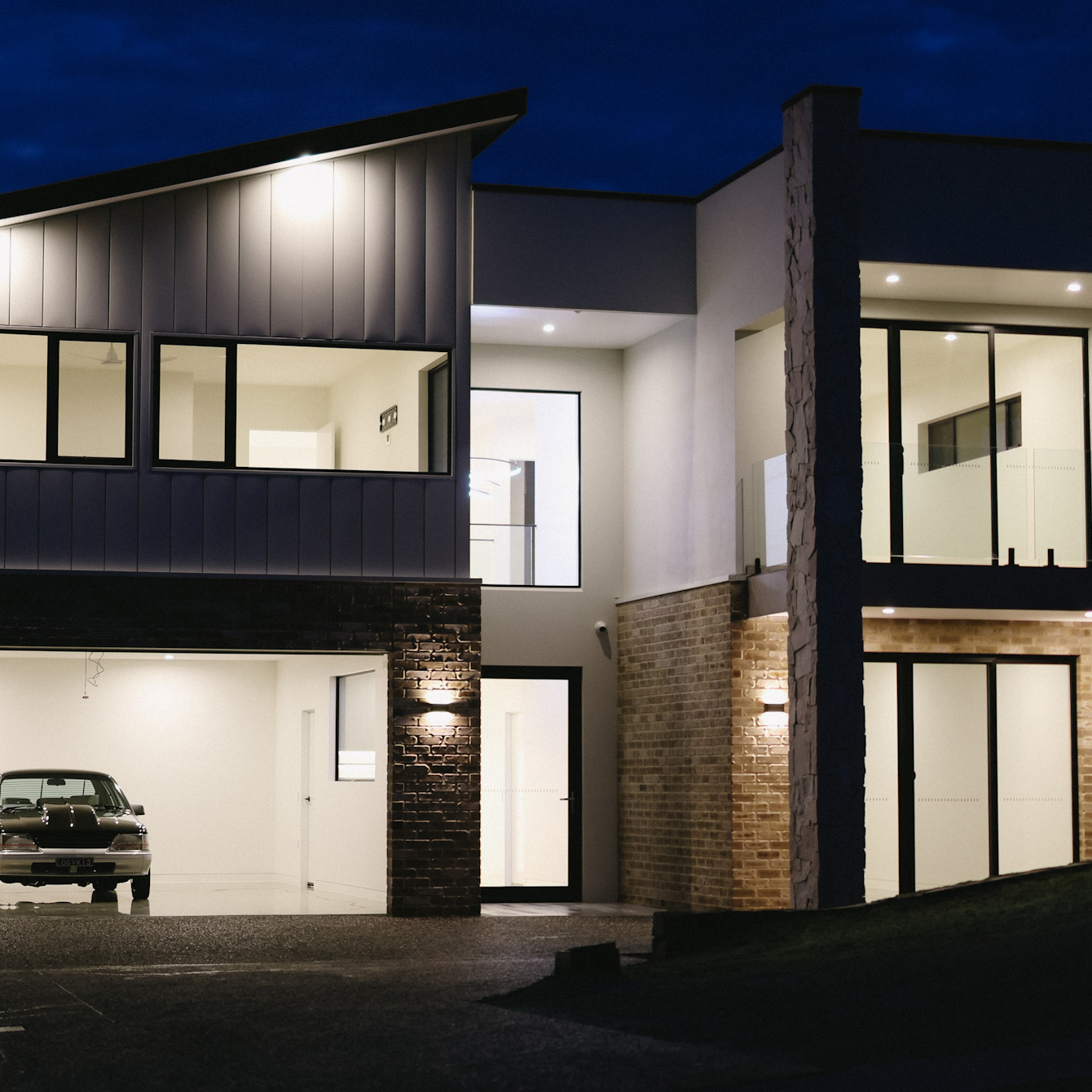Modern two-storey home with illuminated façade at night.
